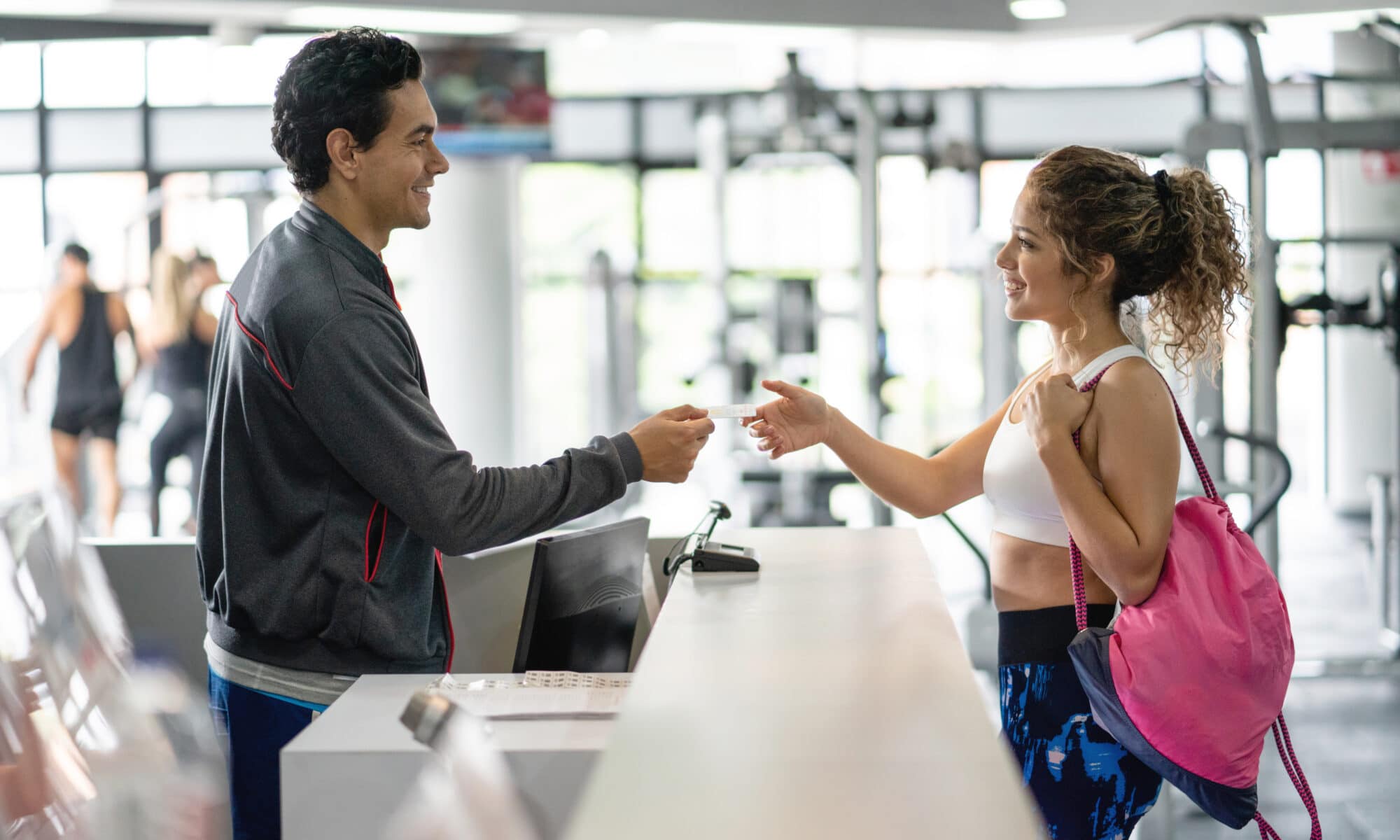 Gym and Fitness POS Point of Sale Cheerful employee at the gym handing a credit card back to female customer